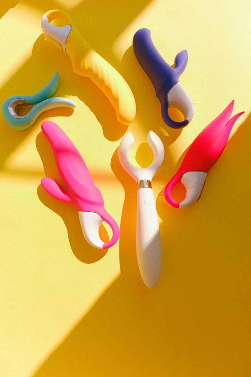 A playful image of modern dildos in various shapes, colors, and sizes, possibly displayed with a vintage historical backdrop to contrast the old and new.